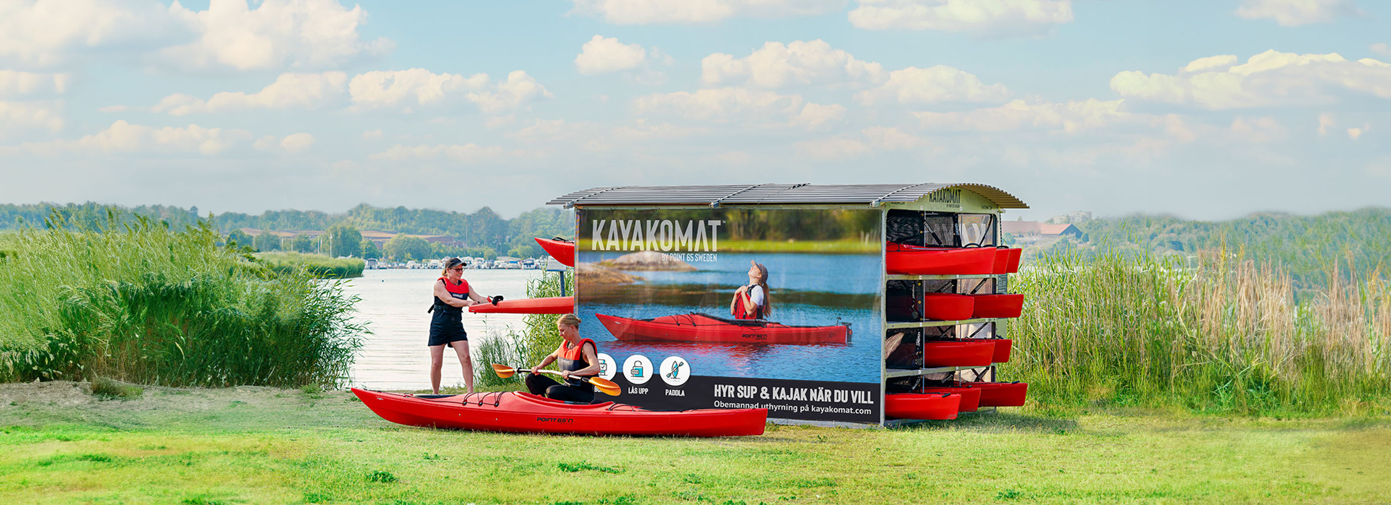 En KAYAKOMAT-station med kajaker och paddlare vid vattnet